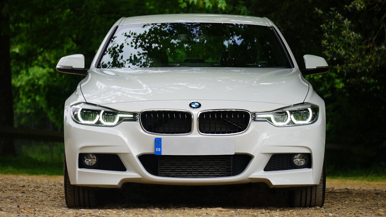 Elegant white luxury car with prominent grille and sleek design, set outdoors, showcasing modern headlights.
