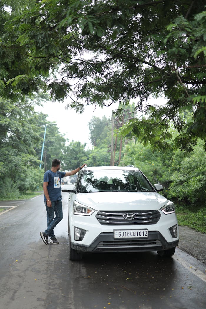 A man stands beside a white car on a green, tree-lined road. Perfect for outdoor and travel themes.